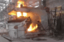 Electric arc furnace (EAF) in operation with molten metal pouring and intense flame emission